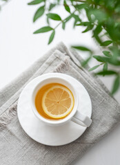 A cup of tea with lemon, napkin and green branch on a white table.