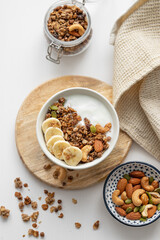 Granola with banana and nuts on a wooden board on a white table with a napkin.