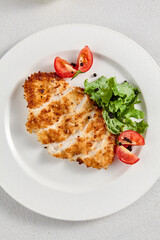 Crispy breaded chicken fillet served with fresh greens and tomato slices, suitable for restaurant menus and recipe blogs