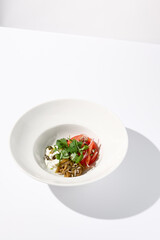 Artful salad with tomatoes, stracciatella cheese, and eggplants garnished with cilantro on a modern white bowl