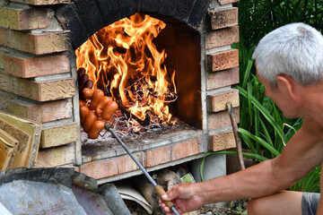 Man roasts meat sausages in a brick fireplace at the cottage