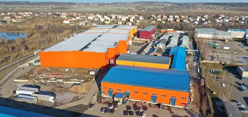 Complex of huge warehouses outside the city limits for storage of goods of retail chains in fall, winter in Europe. An aerial view of the orange and blue logistics center.