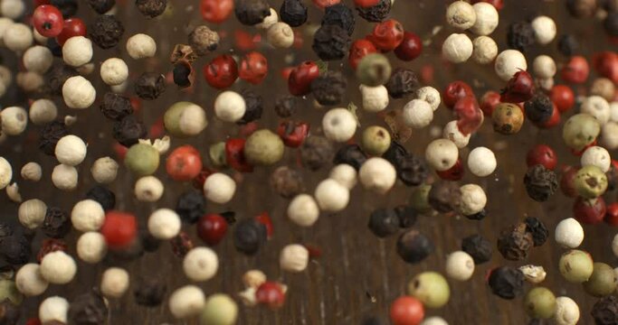 Super slow motion macro of dry mixed flavorful and aromatic peppercorn seeds is flying isolated on soft rustic wood background at 1000fps.