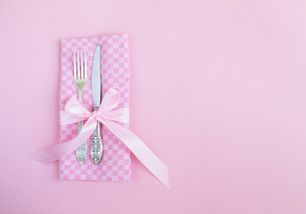 Pink napkin, knife and fork on the pink background. Holiday table setting. Top view. Copy space.