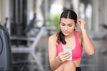 Athletic female in workout attire engaged with mobile device amidst gym equipment.