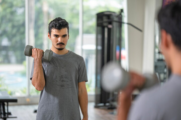 Intense concentration is captured as a man performs bicep curls with dumbbells, highlighting the discipline of personal fitness training. Discipline in strength training concept..