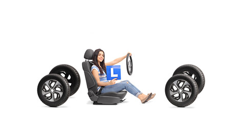Young woman holding a learner plate and a steering wheel seated on a car seat and four tires