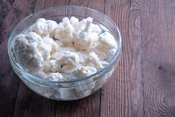 Cauliflower inflorescences in a glass cup with water. Cauliflower background. Cauliflower on a wooden table.