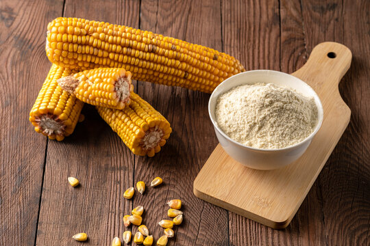 Cornmeal in a cup and dry cobs on a wooden table.