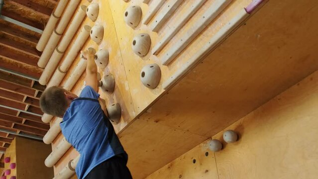 Boy engages in campus board training using wooden sticks for climbing. Child repeats basic patterns of movement for climbing