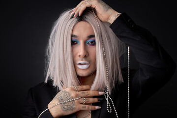 Guy in blonde wig posing like fashion model, pretend to be homosexual, transvestite, gay, lgbtq member. beauty industry, fashion, style. feminine male model with make-up on face isolated om black - obrazy, fototapety, plakaty