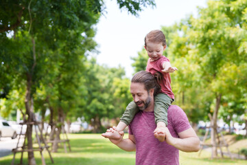 Fototapeta premium Handsome Caucasian man, taking my little son play in garden on nice day, son was placed on neck, little boy placed arms on father's head, father held onto cute son's legs for safety.
