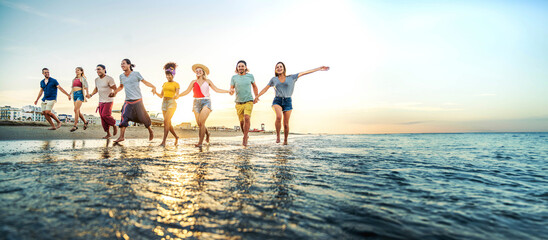 Crowd of friends running to sunset sea - Summer holidays concept with guys and girls enjoying beach sunrise - Happy young people with arms up standing on coastline - Colorful background photo