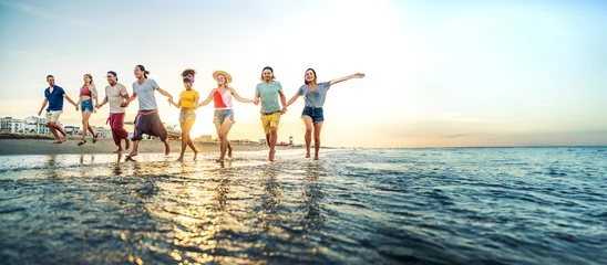 Poster Crowd of friends running to sunset sea - Summer holidays concept with guys and girls enjoying beach sunrise - Happy young people with arms up standing on coastline - Colorful background photo © Davide Angelini