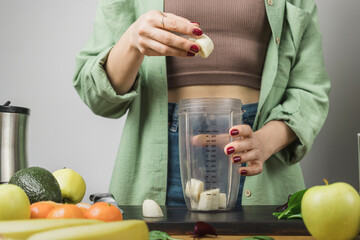 Woman holding banana pieces, preparing healthy vegan smoothie with spinach, apple and avocado in a...