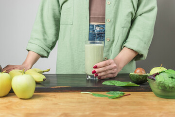 Unrecognizable woman in casual wear holding glass of fresh blended healthy green vegan smoothie....