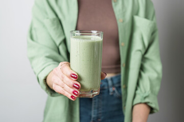Unrecognizable woman in casual wear holding glass of fresh blended healthy green vegan smoothie