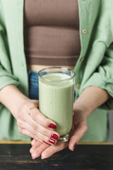 Unrecognizable woman in casual wear holding glass of fresh blended healthy green vegan smoothie