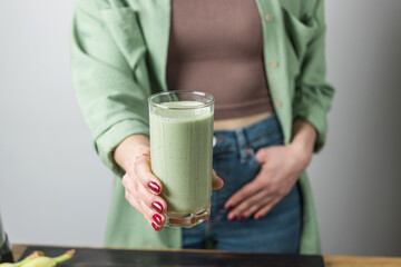 Unrecognizable woman in casual wear holding glass of fresh blended healthy green vegan smoothie