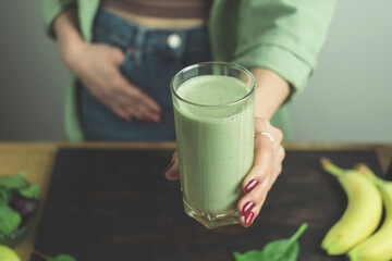 Unrecognizable woman in casual wear holding glass of fresh blended healthy green vegan smoothie....