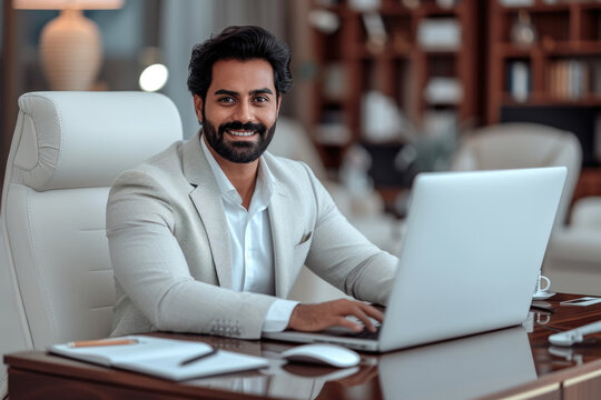 Confident Indian businessman working on laptop while sitting at the table in office