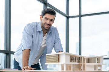 Smiling caucasian architect engineer looking at camera while standing with house model. Smart interior designer standing while holding pencil. Project plan, civil engineering, worker. Tracery.