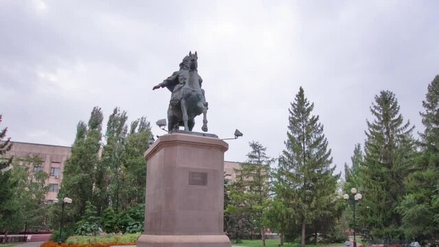 Timelapse Hyperlapse of Monument in Uralsk. A Stroll Through the Pedestrian Zone in the City Center Under a Cloudy Sky, Celebrating the Historical Legacy in Kazakhstan