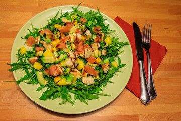 Fresh healthy salad with mango, avocado, salmon, arugula and croutons on wooden table