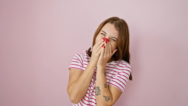 Cheerful young brunette girl sporting a stripe tshirt bursts into gleeful laughter, coyly covers mouth with hand over a scandalous gossip, exuding pure joy on isolated pink background.