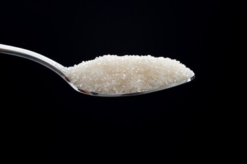 Spoon with sugar crystals on black background