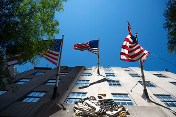 Three American flags flutter in the wind above a classical sculpture on a building facade under a...