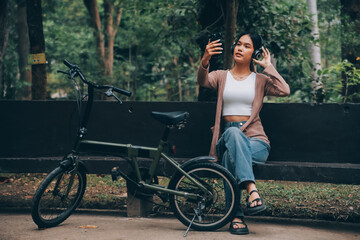 Naklejka premium Happy young Asian woman while riding a bicycle in a city park. She smiled using the bicycle of transportation. Environmentally friendly concept.