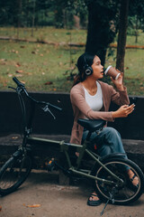 Naklejka premium Happy young Asian woman while riding a bicycle in a city park. She smiled using the bicycle of transportation. Environmentally friendly concept.