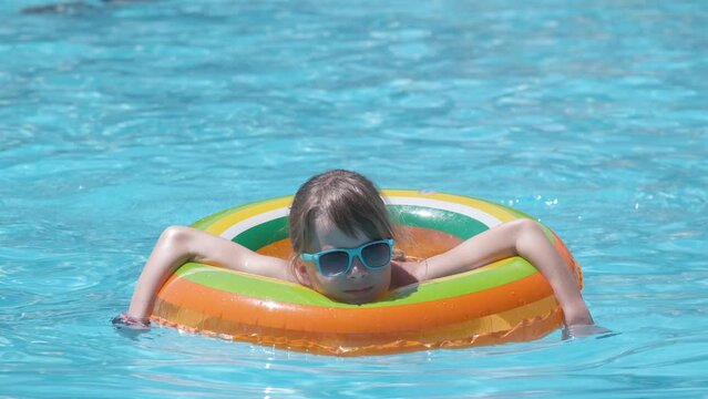 Happy child girl swimming on inflatable circle in swimming pool on sunny summer day during tropical vacations