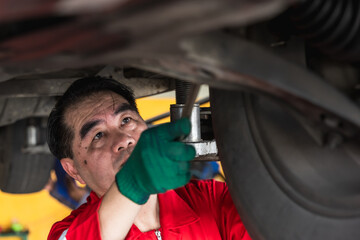 Fototapeta premium Asian mechanic working underneath car and changing engine in auto repair shop