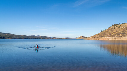 Lonely rower in a coastal rowing shell - Carter Lake in fall or winter scenery in northern Colorado.
