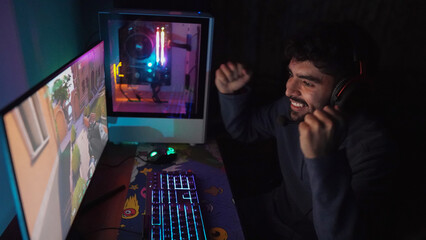 bearded man celebrates victory in shooter video game with his high-tech computer and colorful video game room
