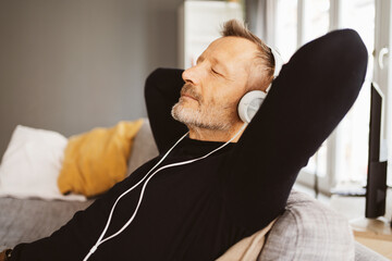 Relaxed Bestager Man Sitting on Sofa with Closed Eyes, Listening to Music with Headphones - 725792314