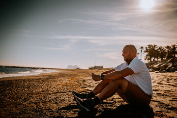 Sotogrante, Spain - January 25, 2024 - A man sits on a sandy beach looking contemplative, ocean waves and palm trees in the background.