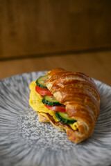 a croissant filled with vegetables on a grey plate on a wooden background