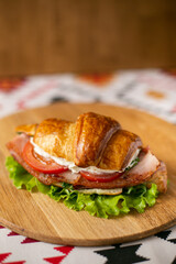 Croissant filled with bacon and tomatoes on a wooden background