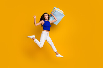 Full length photo of lucky cool woman wear blue top jumping high holding bargains isolated yellow...