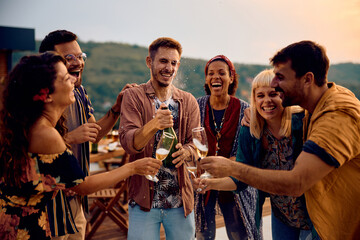 Happy friends having fun while opening champagne on party at sunset. © Drazen