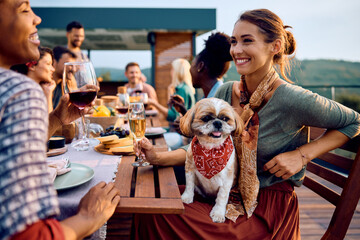 Happy woman with dog talking to her friend at dining table on terrace.