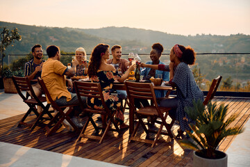 Group of happy diverse friends toasting at dining table on patio at sunset.