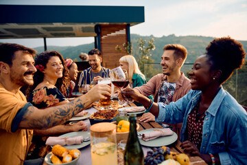 Happy friends toasting while gathering for meal on terrace at sunset. - obrazy, fototapety, plakaty