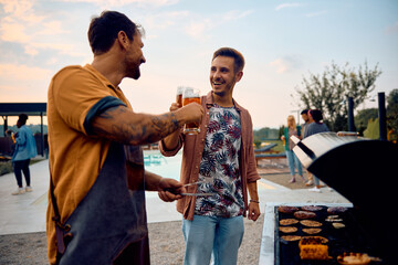 Happy men toasting with beer while making barbecue outdoors.