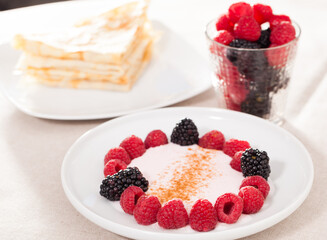 Breakfast of raspberries and blackberries with yogurt and pancakes on table