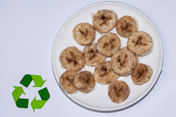 A plate with slices of bananas and chips that are black in color, that is, they are almost spoiled, they stand on a white background, as a sign of its recycling.