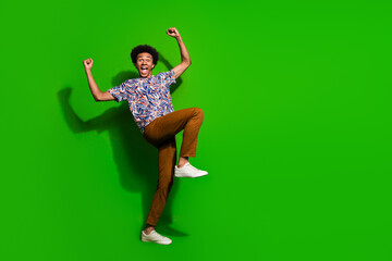 Fulll length photo of lucky cheerful guy wear print shirt yelling yes rising fists empty space isolated green color background